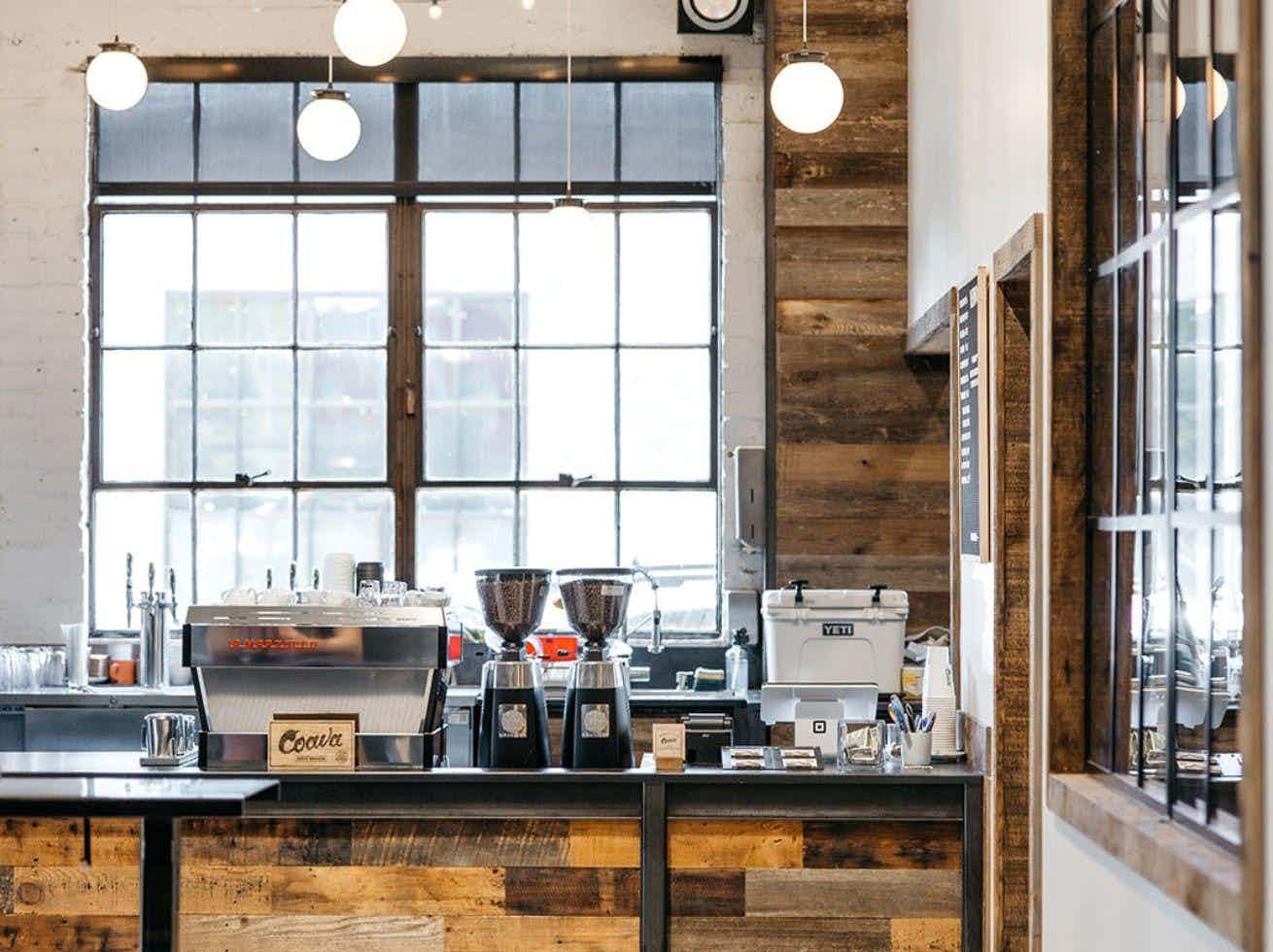  Coffee bar framed by large industrial windows and wood paneling, with espresso machines and grinders on display.