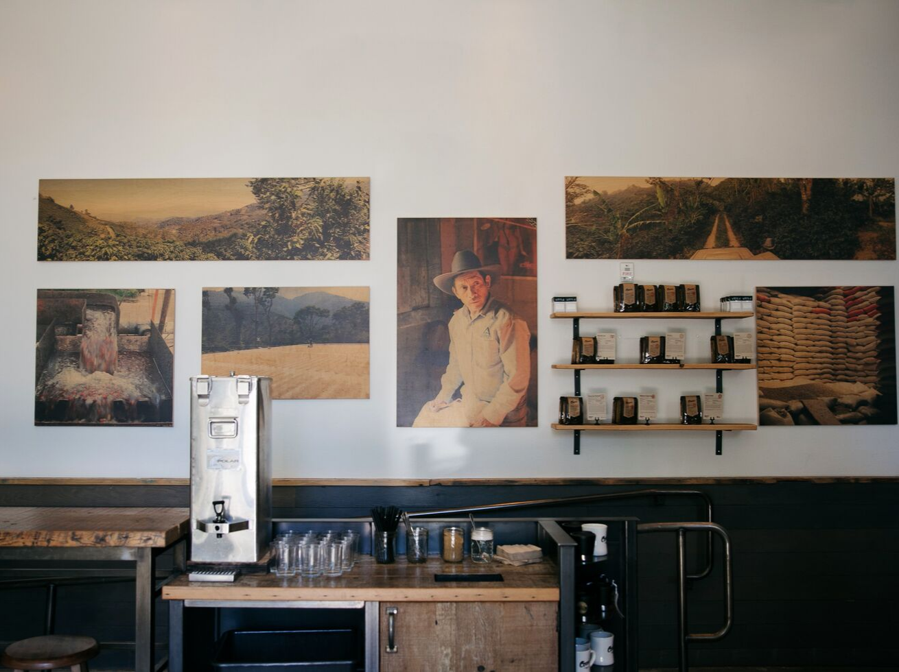 Gallery wall of framed artwork above a minimalist water station with stacked cups and carafes.